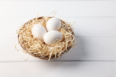 Photo of Raw eggs in basket on white wooden table, closeup