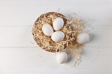 Photo of Raw eggs in basket on white wooden table, top view