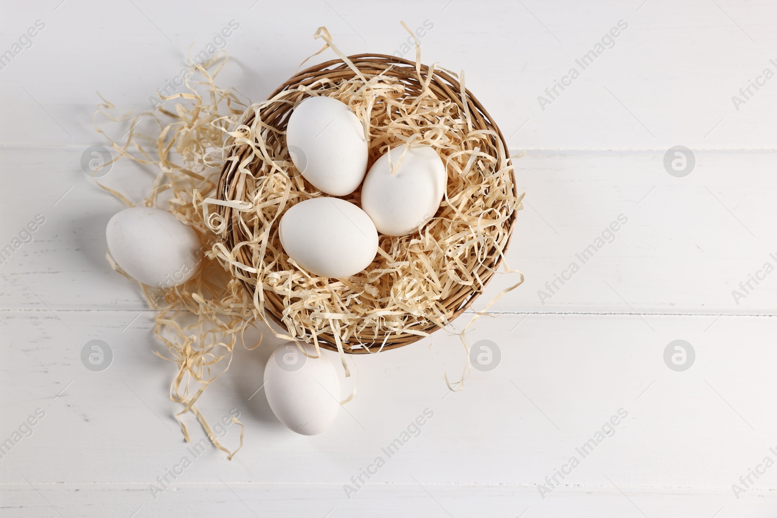 Photo of Raw eggs in basket on white wooden table, top view