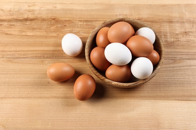 Photo of Raw eggs in bowl on wooden table, closeup