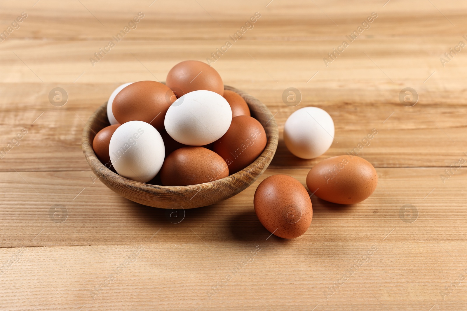 Photo of Raw eggs in bowl on wooden table, closeup