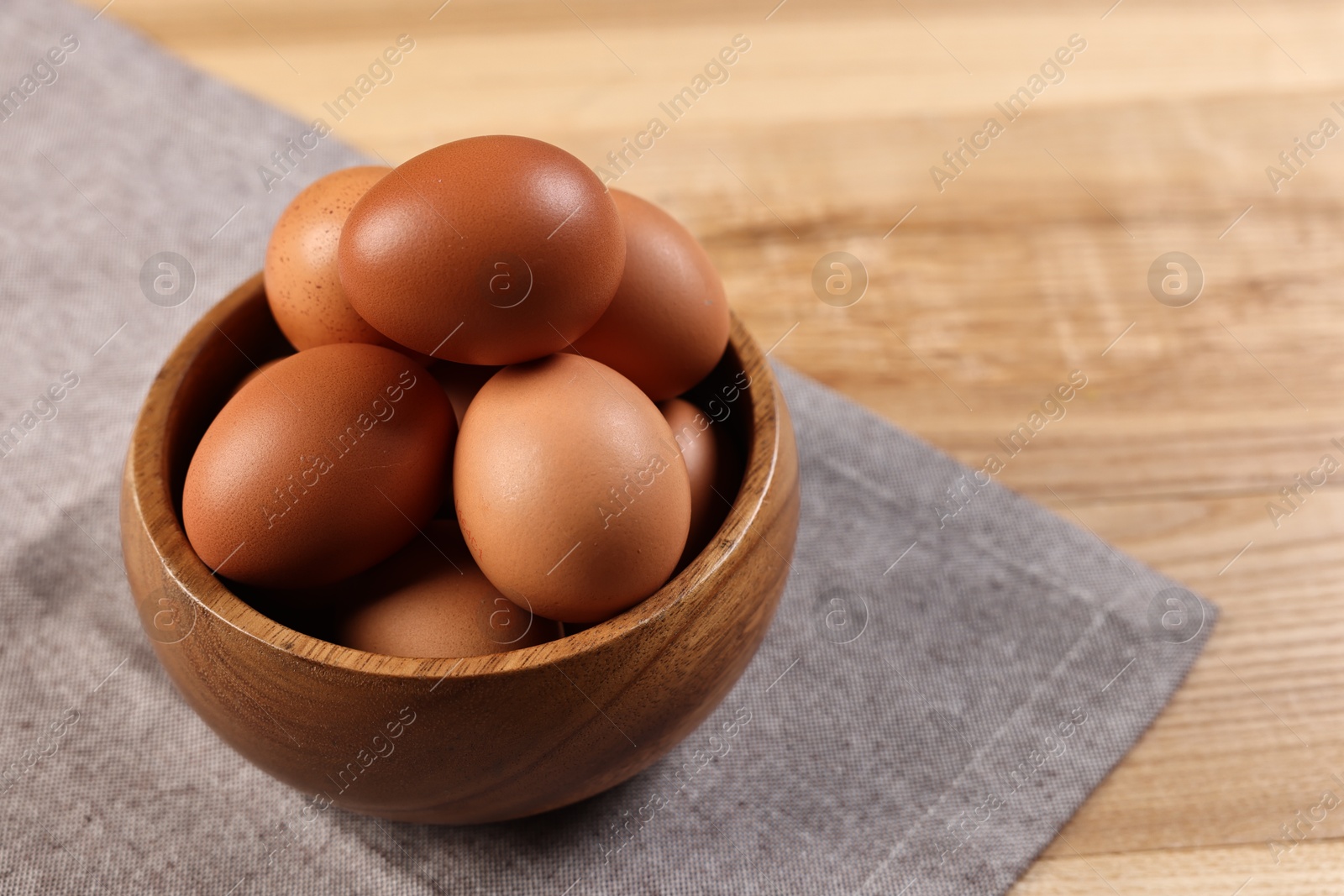 Photo of Raw eggs in bowl on wooden table, closeup. Space for text