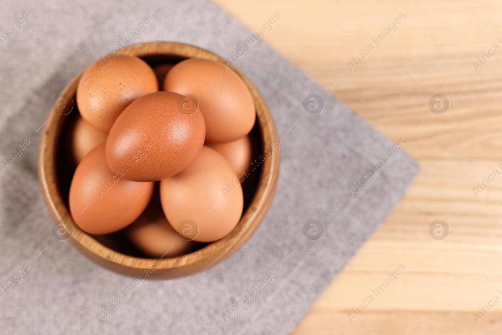 Photo of Raw eggs in bowl on wooden table, top view