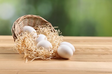 Photo of Basket with raw eggs on wooden table, closeup. Space for text