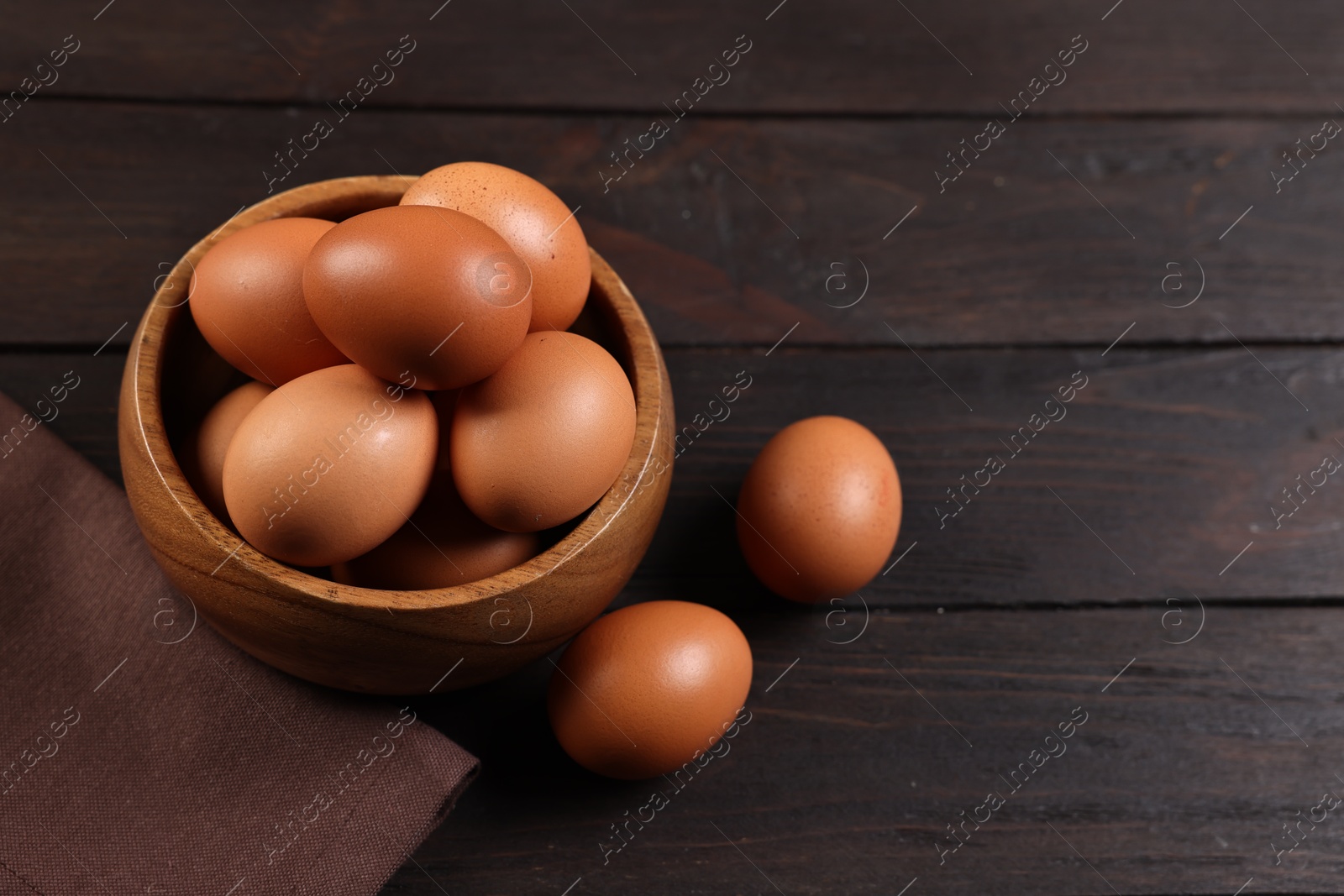 Photo of Raw eggs in bowl on wooden table, closeup. Space for text