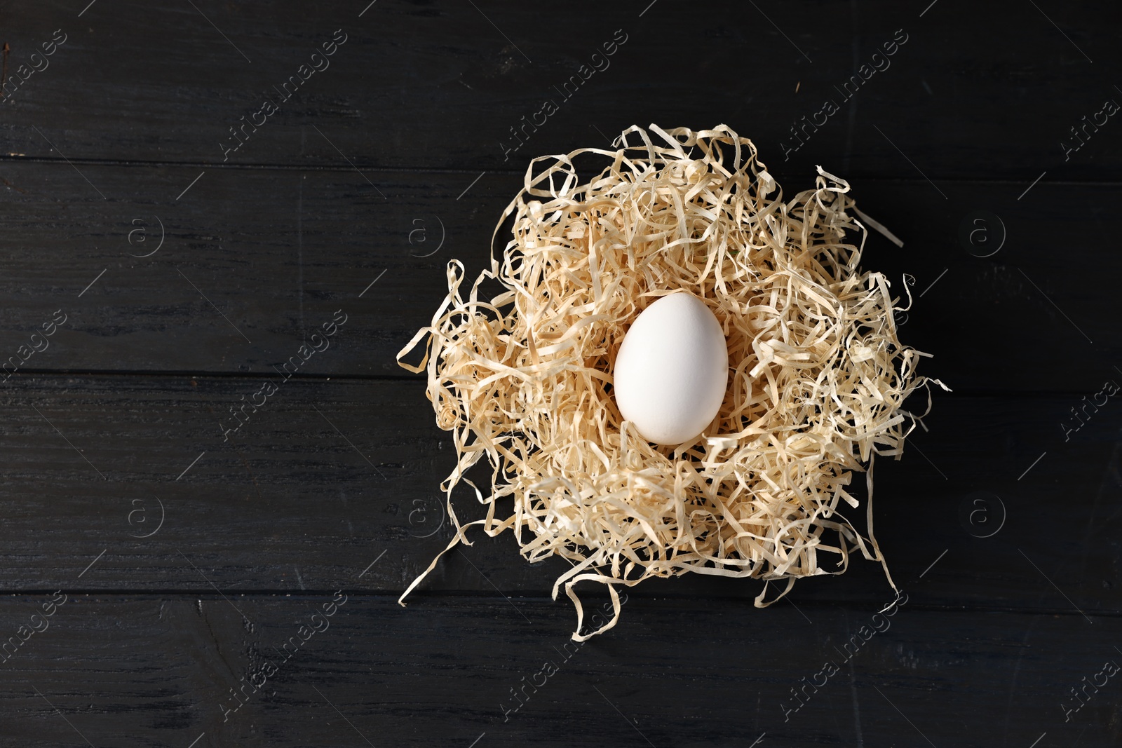 Photo of Raw egg in nest on black wooden table, top view. Space for text