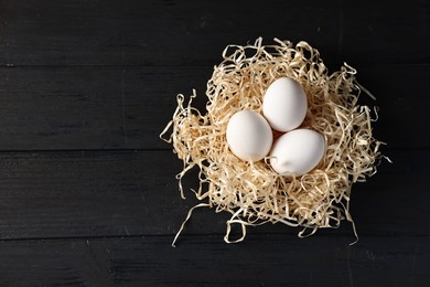 Photo of Raw eggs in nest on black wooden table, top view. Space for text