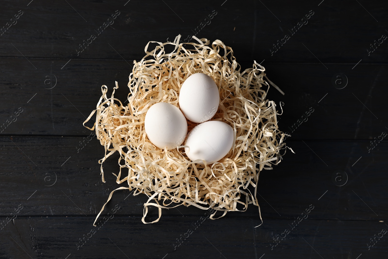 Photo of Raw eggs in nest on black wooden table, top view