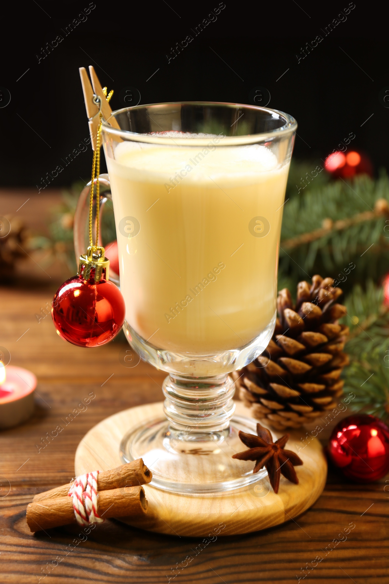 Photo of Tasty Christmas cocktail (eggnog) in glass, festive decor and burning candle on wooden table, closeup