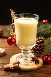 Photo of Tasty Christmas cocktail (eggnog) in glass, festive decor and burning candle on wooden table, closeup