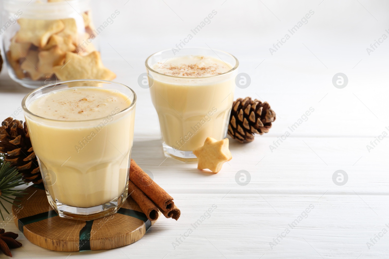 Photo of Tasty Christmas cocktail (eggnog) in glasses, pine cones and spices on white wooden table. Space for text