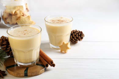 Photo of Tasty Christmas cocktail (eggnog) in glasses, pine cones and spices on white wooden table. Space for text