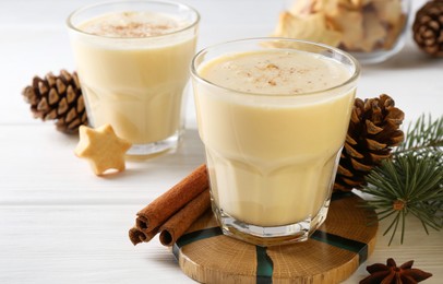 Photo of Tasty Christmas cocktail (eggnog) in glasses, pine cones and spices on white wooden table, closeup