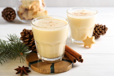 Photo of Tasty Christmas cocktail (eggnog) in glasses, pine cones and spices on white wooden table, closeup