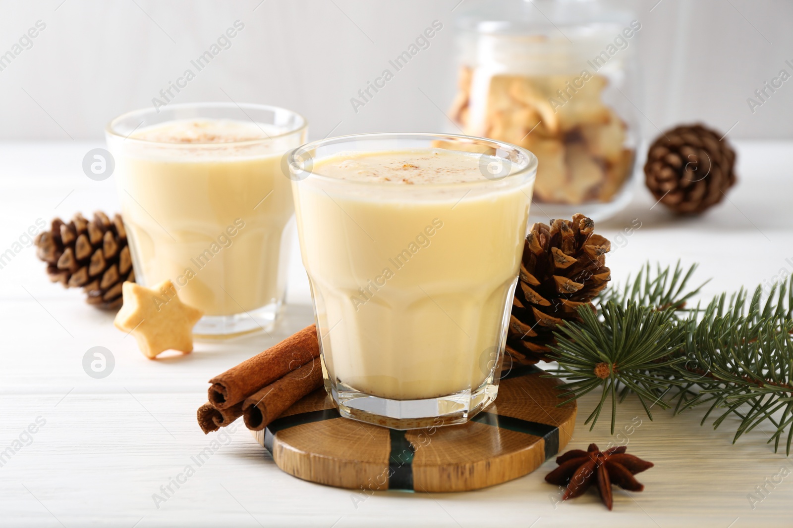 Photo of Tasty Christmas cocktail (eggnog) in glasses, pine cones and spices on white wooden table, closeup