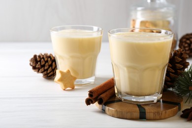 Photo of Tasty Christmas cocktail (eggnog) in glasses, pine cones and spices on white wooden table, closeup