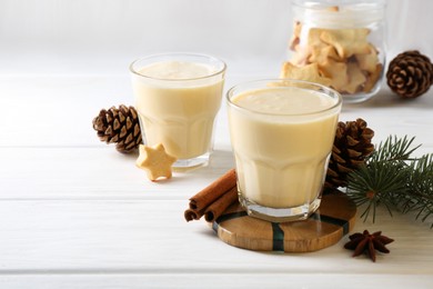 Photo of Tasty Christmas cocktail (eggnog) in glasses, pine cones and spices on white wooden table