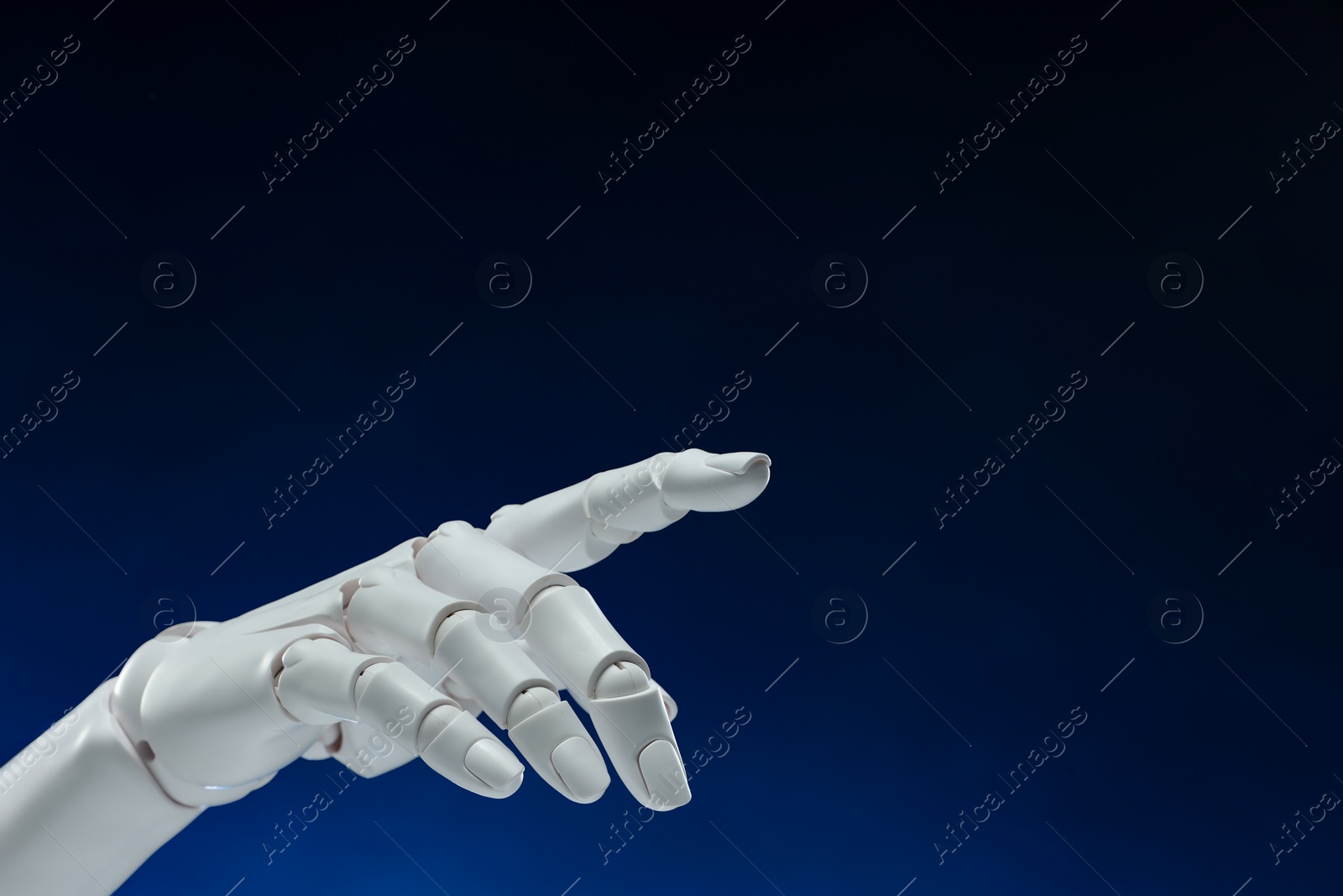 Photo of Artificial intelligence. Robot hand pointing at something on dark blue background, space for text