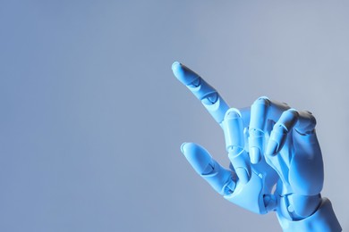 Photo of Artificial intelligence. Robot hand pointing at something on pale light blue background, space for text