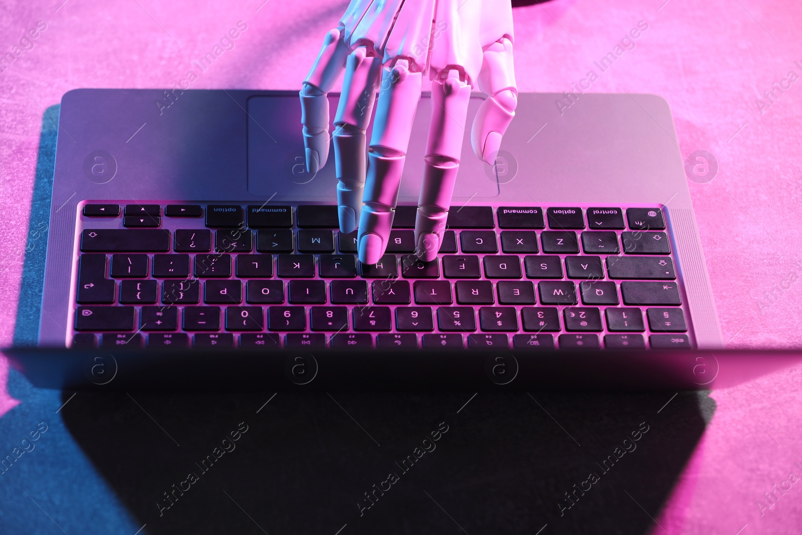 Photo of Artificial intelligence. Robot hand using laptop on table in neon lights, above view