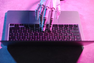 Photo of Artificial intelligence. Robot hand using laptop on table in neon lights, above view