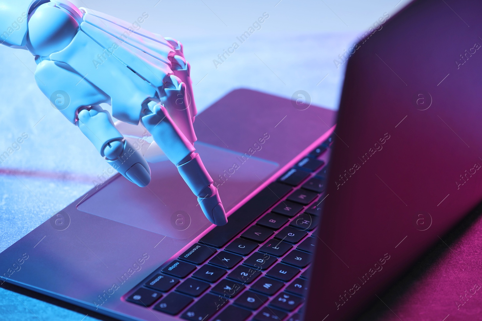 Photo of Artificial intelligence. Robot hand using laptop on table in neon lights, closeup