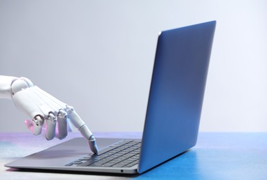 Photo of Artificial intelligence. Robot hand with laptop on table against light grey background