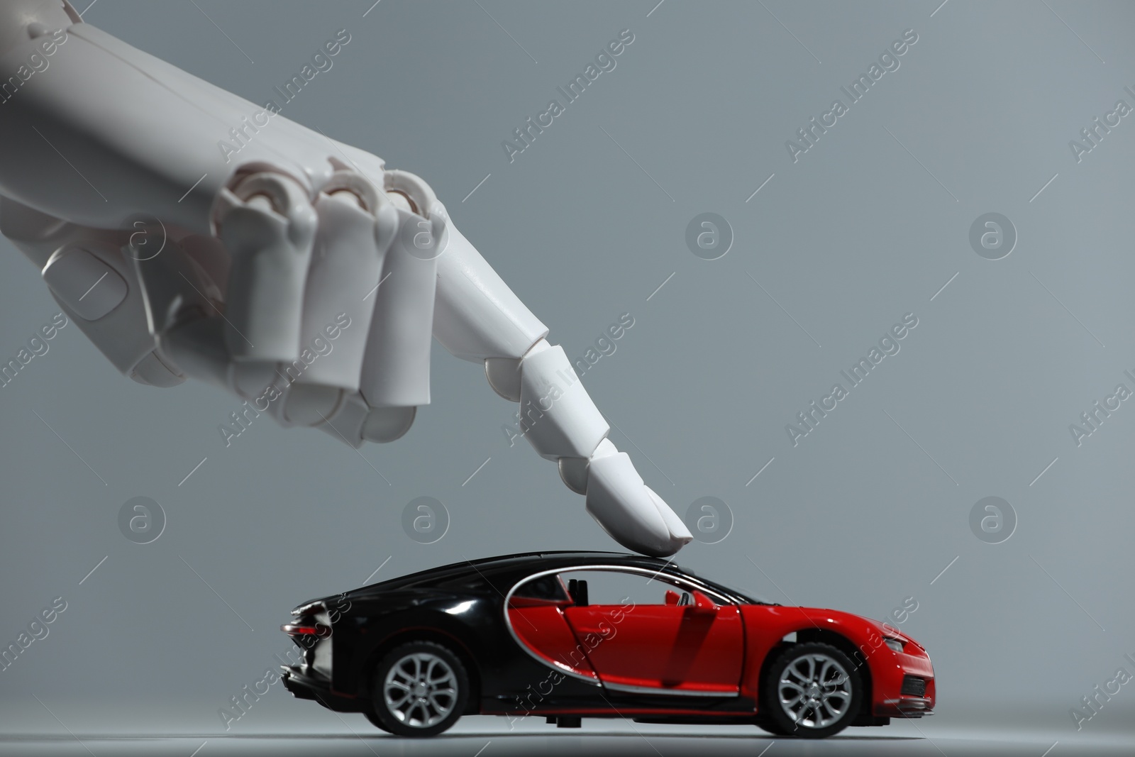 Photo of Artificial intelligence. Robot hand with toy car against grey background, closeup