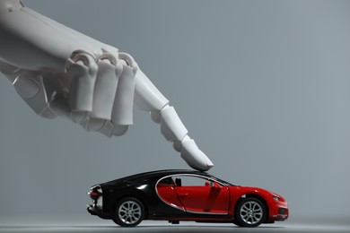 Artificial intelligence. Robot hand with toy car against grey background, closeup