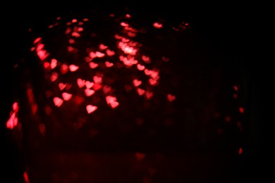 Photo of Romantic decor. Blurred view of heart shaped lights on black background, bokeh effect