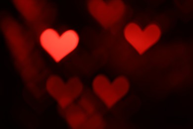 Photo of Romantic decor. Blurred view of heart shaped lights on black background, bokeh effect