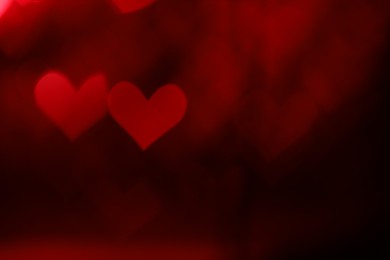 Photo of Romantic decor. Blurred view of heart shaped lights on dark red background, bokeh effect