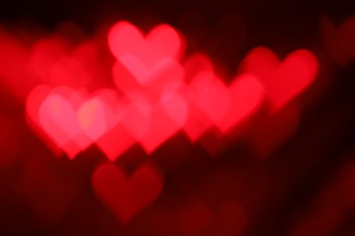 Photo of Romantic decor. Blurred view of heart shaped lights on dark red background, bokeh effect