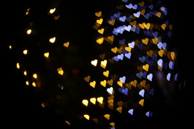 Photo of Romantic decor. Blurred view of heart shaped lights on black background, bokeh effect