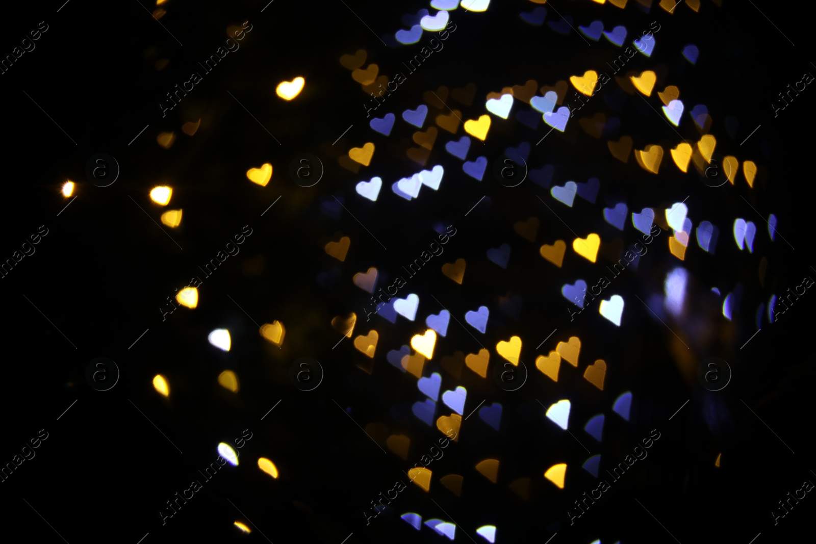 Photo of Romantic decor. Blurred view of heart shaped lights on black background, bokeh effect