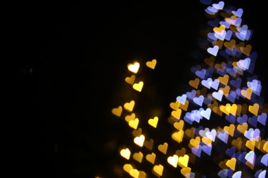 Photo of Romantic decor. Blurred view of heart shaped lights on black background, space for text. Bokeh effect