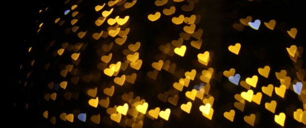 Photo of Romantic decor. Blurred view of heart shaped lights on black background, bokeh effect