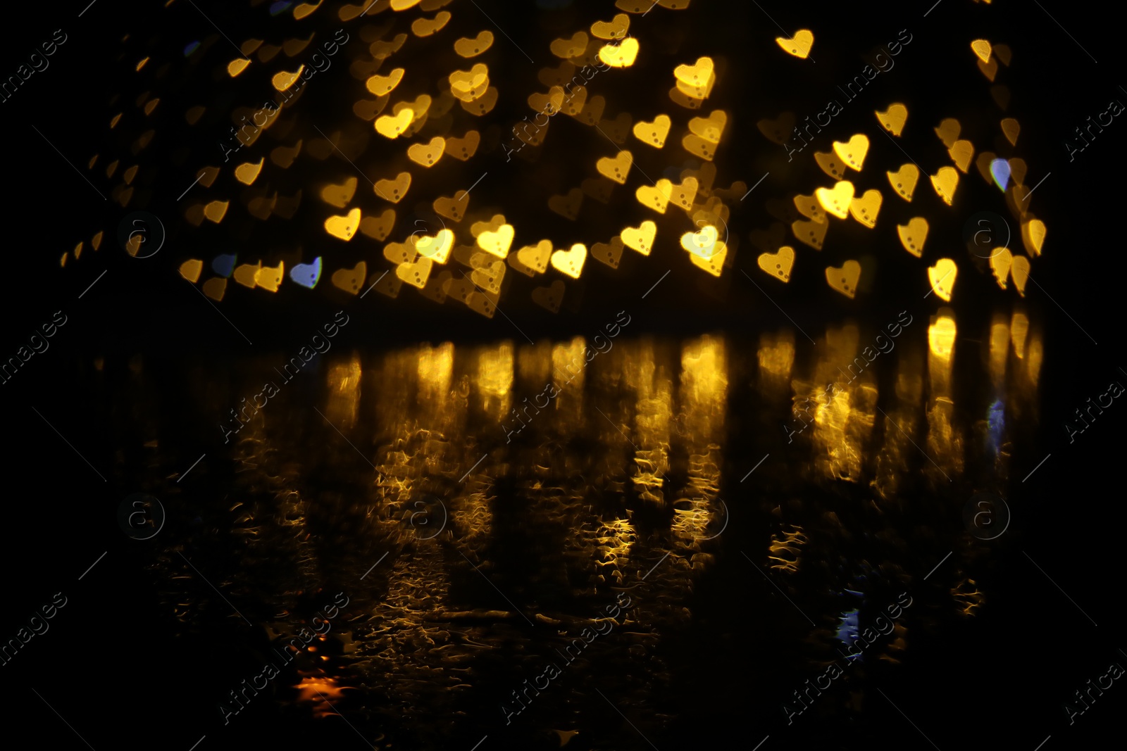 Photo of Romantic decor. Blurred view of heart shaped lights on black background, bokeh effect