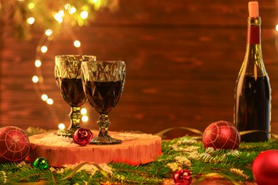 Photo of Red wine and beautiful Christmas decor on wooden table against blurred festive lights. Space for text