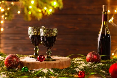 Photo of Red wine and beautiful Christmas decor on wooden table against blurred festive lights. Space for text