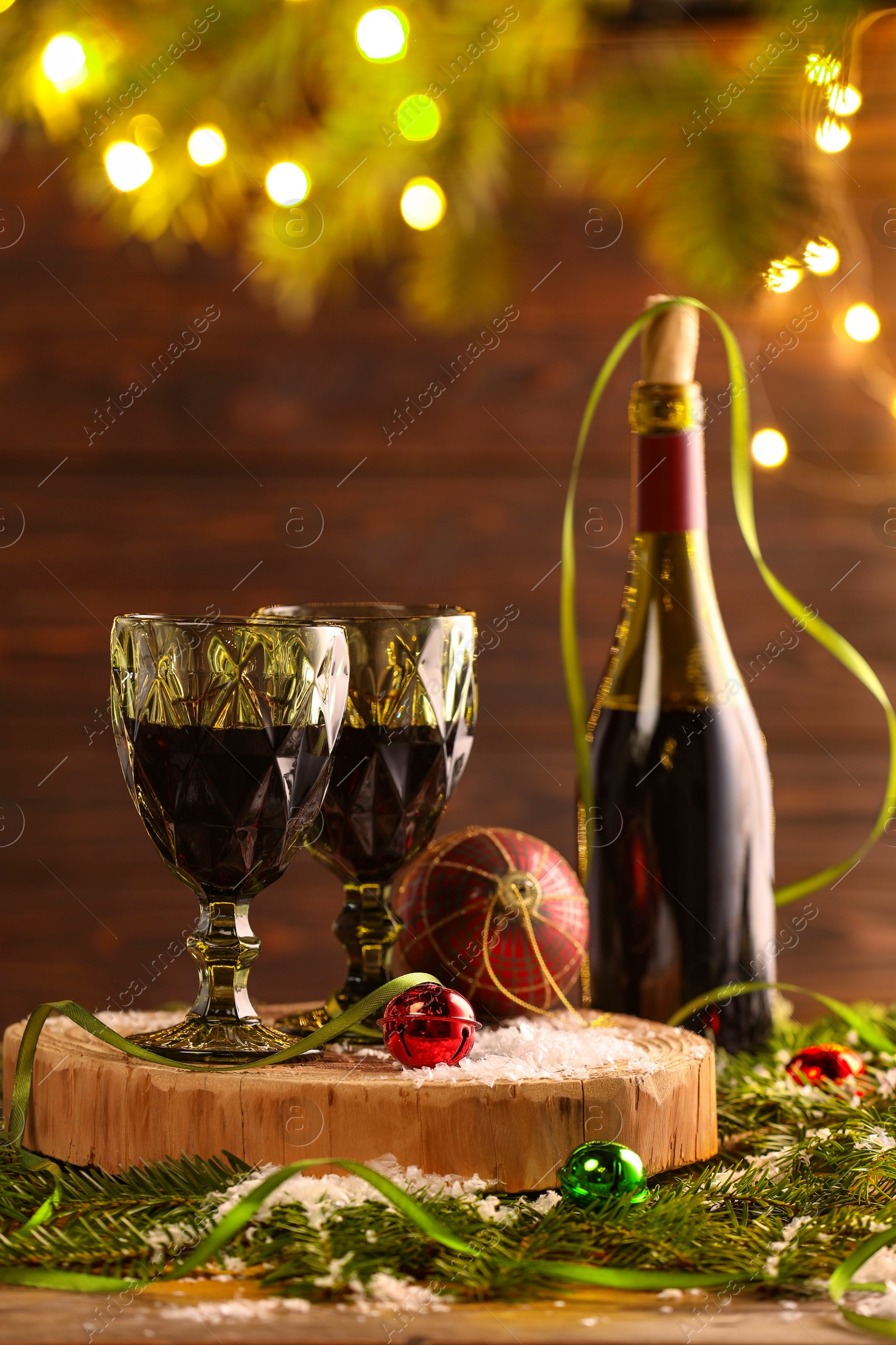 Photo of Red wine and beautiful Christmas decor on wooden table against blurred festive lights