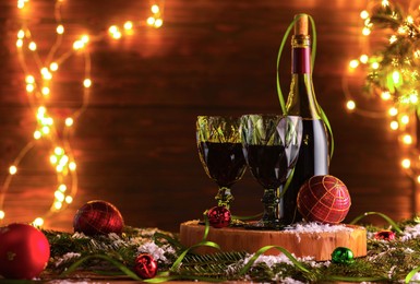 Photo of Red wine and beautiful Christmas decor on wooden table against blurred festive lights. Space for text