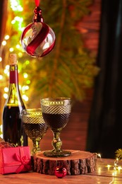 Photo of Red wine and beautiful Christmas decor on wooden table against blurred festive lights. Space for text