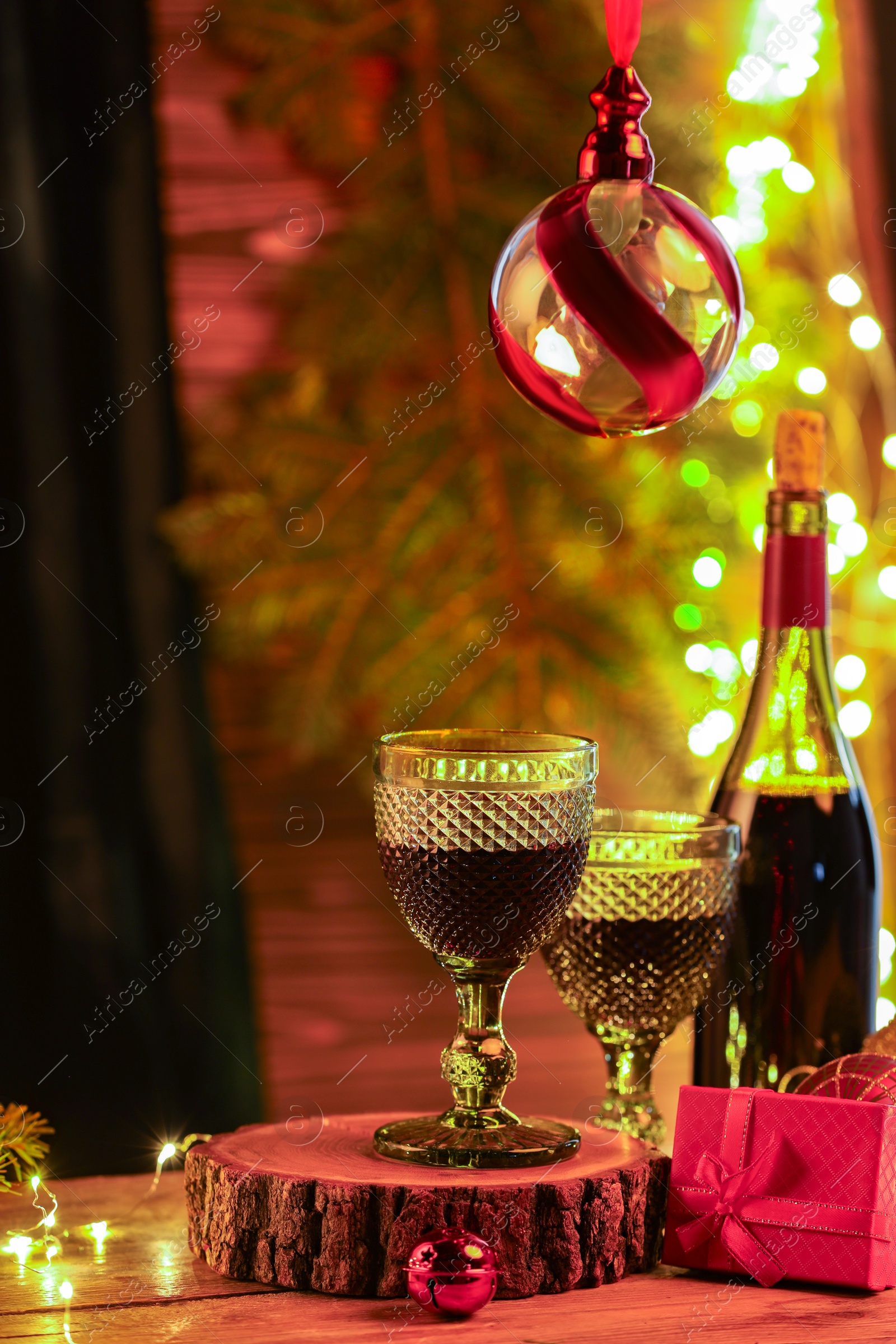 Photo of Red wine and beautiful Christmas decor on wooden table against blurred festive lights. Space for text