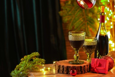 Photo of Red wine and beautiful Christmas decor on wooden table against blurred festive lights. Space for text