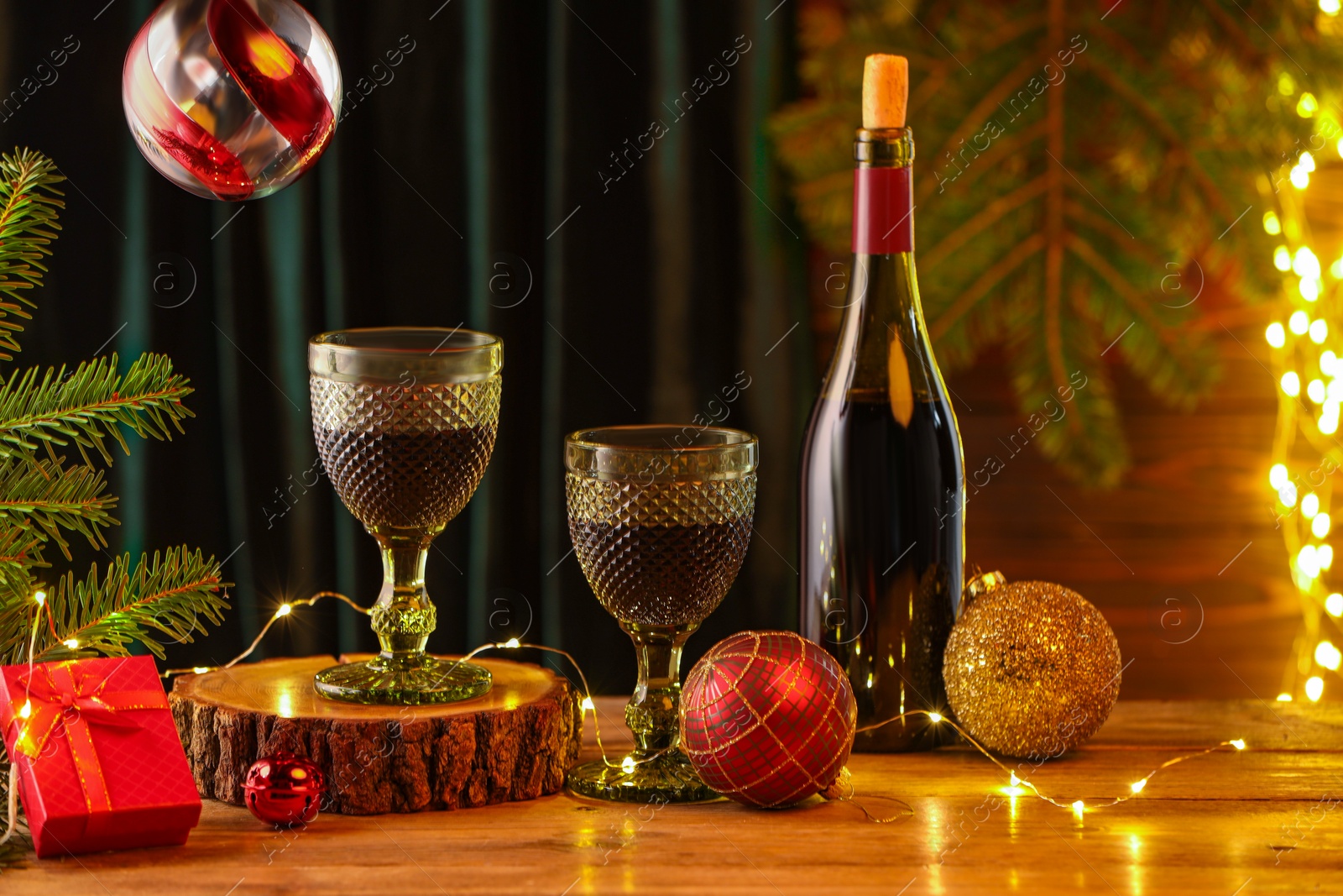 Photo of Red wine and beautiful Christmas decor on wooden table against blurred festive lights