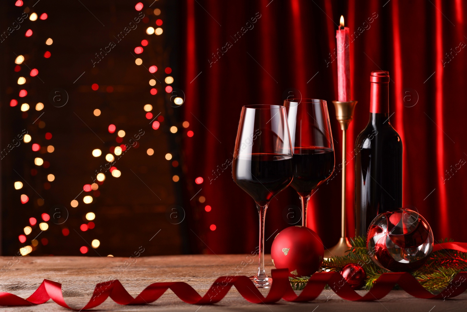 Photo of Red wine, Christmas ornaments and fir branch on wooden table against blurred festive lights. Space for text