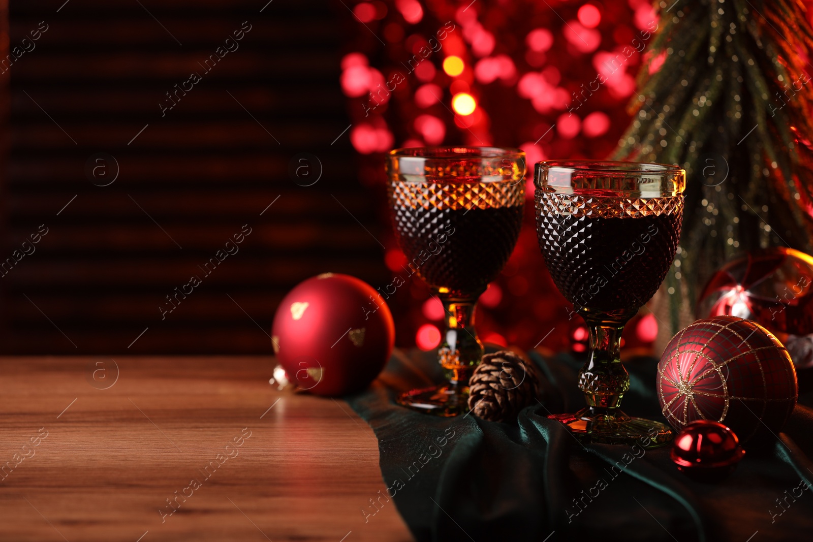 Photo of Glasses with red wine and beautiful Christmas decor on wooden table, closeup. Space for text