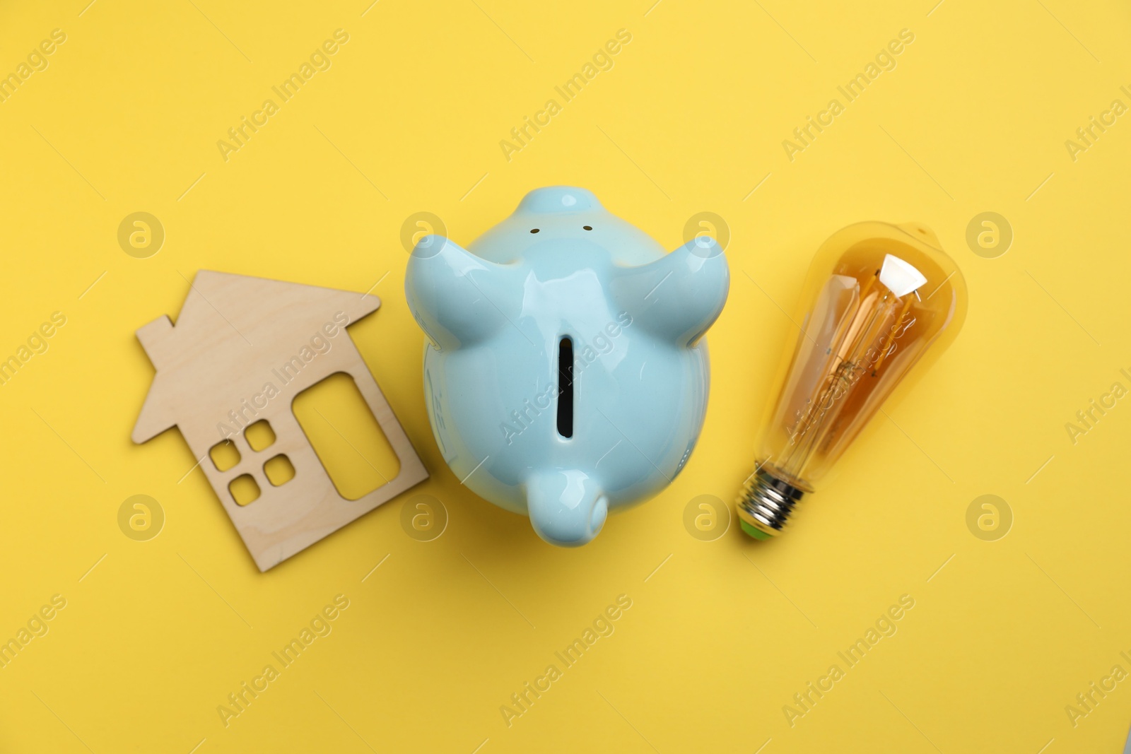 Photo of Piggy bank, light bulb and house model on yellow background, flat lay. Energy saving concept