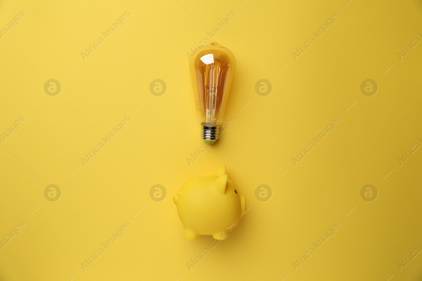 Photo of Light bulb and piggy bank on yellow background, flat lay. Energy saving concept